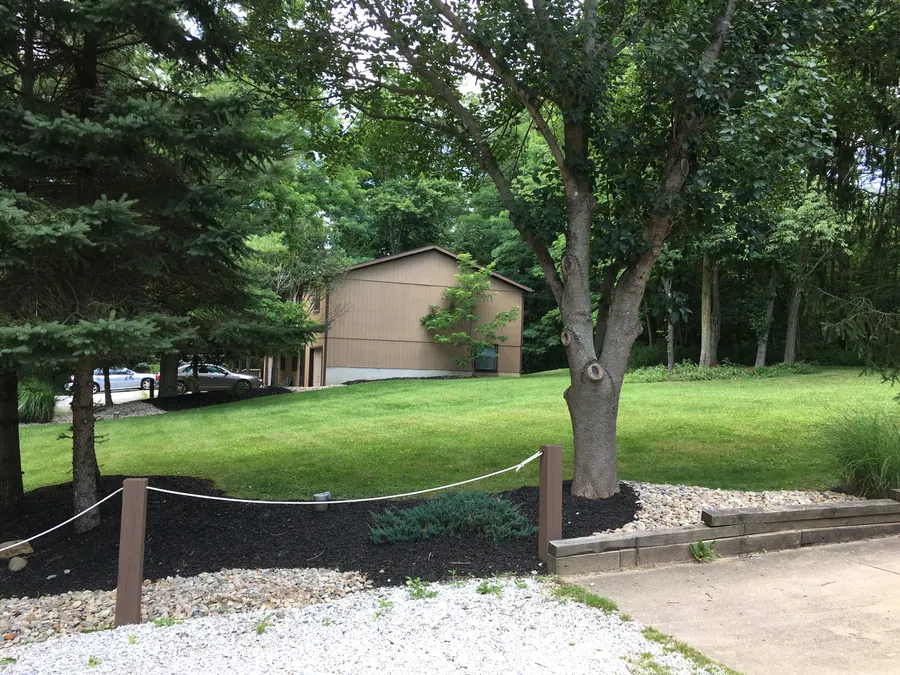 Green lawn and mature trees beside a Hidden Pines townhome