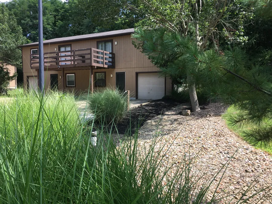 Brown Hidden Pines townhome with a balcony and garage, framed by pine trees